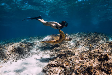 Woman freediver glides underwater with sea turtle.