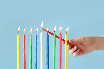 Woman lighting candles for Hanukkah on color background
