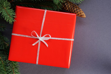 Christmas red gift box with silver ribbon, green natural pine tree branch with pine cone