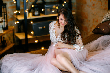 Naklejka premium Happy pregnant woman sitting on bed and touching her belly.