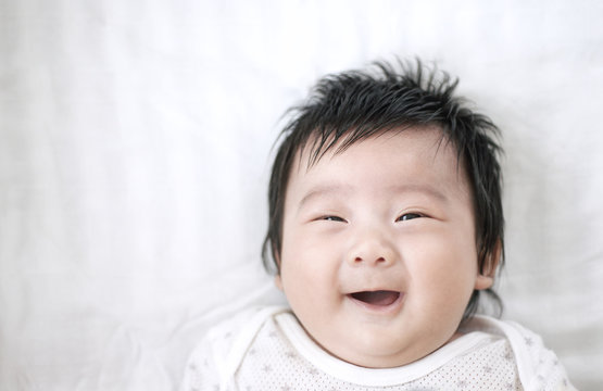 Cute adorable baby asian boy looking at camera and smiling on white bed : Closeup