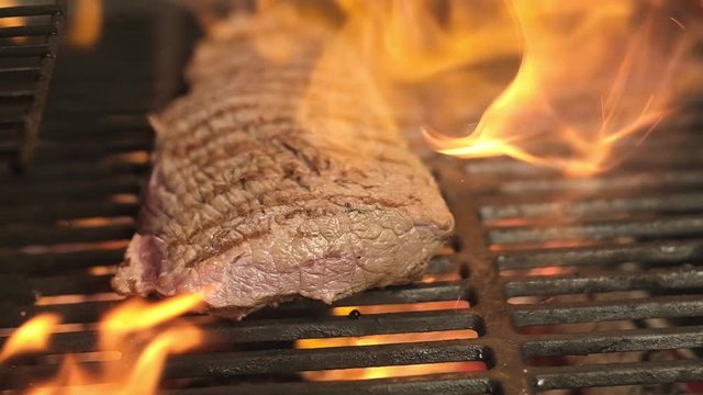 big juicy piece of raw meat on a hot grill on an open flame. Pork or beef cooked on the grill in the center of the frame. Barbecue in nature. Meat fillet is fried on fire on a cast iron grill.