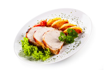 Roasted pork with baked potatoes and vegetables on white plate