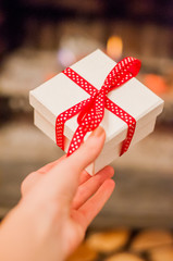 Close up shot of female hands holding a small gift wrapped with red ribbon. Small gift in the hands of a woman indoor. Female Holding Rustic Decorated Gift with Red  Ribbon