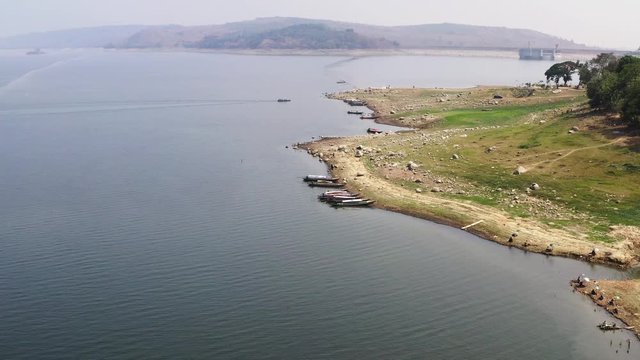 Aerial along dry shore of island with boats along coast, dolly in
