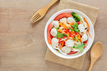 top view of spicy fish ball salad in a bowl on wooden table. delicious thai style food menu.