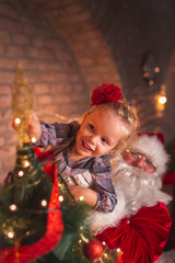 Fototapeta na wymiar Little girl and Santa placing Christmas tree topper