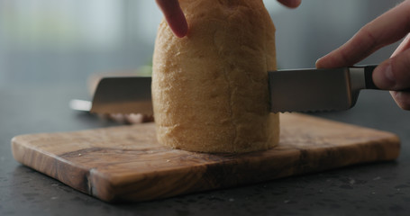 man cuts ciabatta bread on olive board