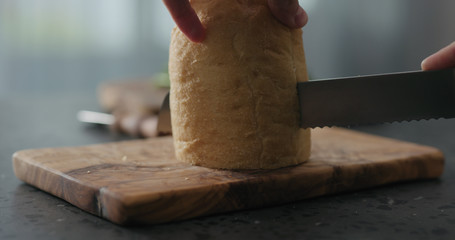 man cuts ciabatta bread on olive board