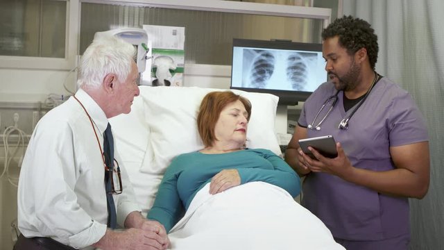 A male nurse delivers bad news to an older couple at the hospital. Reviewing test results on a tablet computer at the bedside.