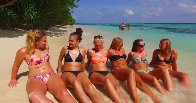 Group of happy women sitting on white beach, showing each other moments of holidays spent on tropical islands of Hawaii