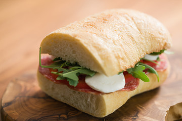ciabatta sandwich with salami and mozzarella cheese on walnut table