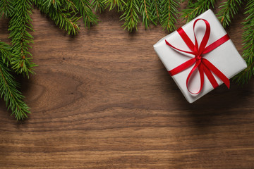 Top view of green spruce twigs with gift box with red ribbon on walnut wood surface