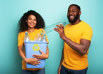 Happy couple hold a plastic container with bottles over a light blue color. Concept of ecology,...