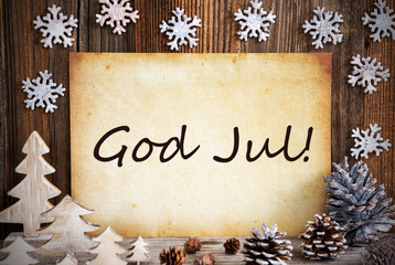 Fototapeta na wymiar Old Paper With German Text God Jul Means Merry Christmas. Christmas Decoration Like Tree, Fir Cone And Snowflakes. Brown Wooden Background