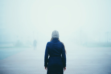 Girl in a warm blue coat and hat in a foggy city