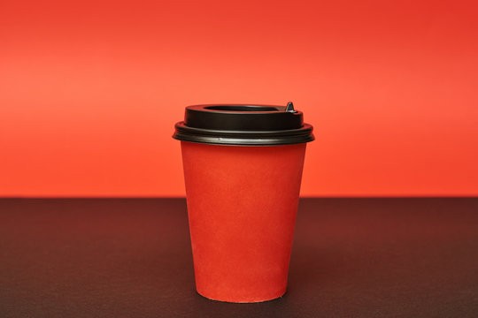 Red disposable paper cup for takeaway drinks. Mockup red paper cup on red and black background.