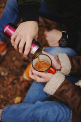 romantic couple, a guy and a girl walk in the autumn cold forest and drink tea