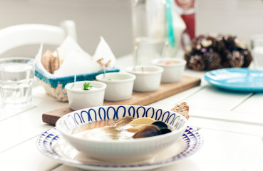 Seafood soup with mussels, prawns and fish in white bowl with blue ornament with sauce in small bowls for traditional meze dinner on the wooden table on background.