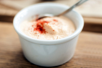 White yogurt sauce with paprika in small bowl for traditional meze dinner on the wooden table in restaurant.