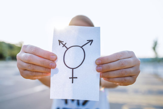 closeup of a young Caucasian woman in the street showing a piece of paper with a transgender symbol drawn in it