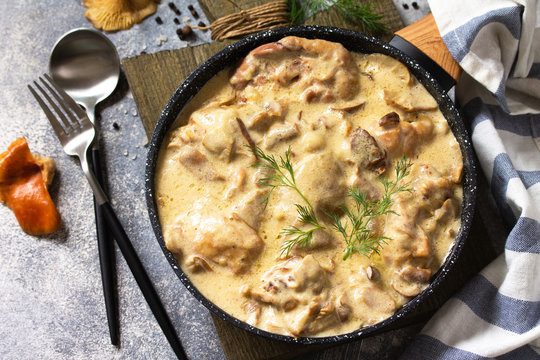 Fricasse - French Cuisine. Chicken stewed in a creamy sauce with mushrooms in a pan on a light stone background.