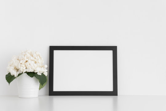 Black frame mockup with a hortensia in a pot on a white table.Landscape orientation.
