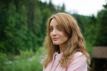 Naklejka premium Attractive young calm blonde woman in pink clothes with long hair on the hill with green forest background during spring or early autumn in the mountains.