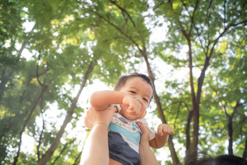 Mom lifting hold infant baby boy in city park against sun light