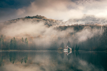 Obraz na płótnie Canvas Foggy day at a lake with a little island with a church in the middle. Mogoasa, Romania.