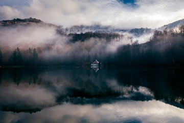 Fototapeta premium Foggy day at a lake with a little island with a church in the middle. Mogoasa, Romania.