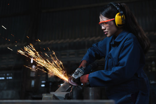 Young diverse female engineer using angle grinder in factory workshop - Ethnic Asian girl working in manufacturing industry job using industrial power tool - Maintenance, production and career concept
