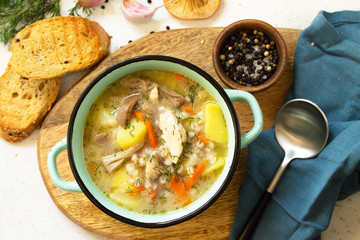 Homemade hot vegetable soup with chicken, mushrooms and bulgur on a white countertop. Top view flat lay background.