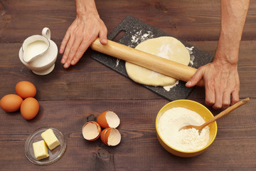 Cook hands rolling dough for baking with rolling pin on the board on a wooden table.