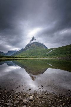 Famous Innerdalen mountain peak reflected in lake bad weather moody scene Norway