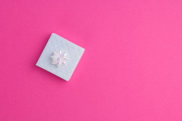 White holographic gift on bright pink background. Invitation, congratulation concept. Top view, flat lay, copy space