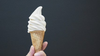 Hand is holding Soft serve ice cream cone with black back ground.