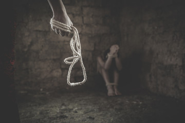 A man standing and holding a chain in his hand, was about to attack a woman sitting in the corner of a dark room.Violence against women, Human rights violations, Human trafficking. - obrazy, fototapety, plakaty