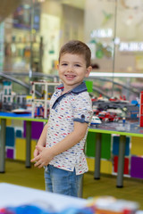 Happy funny little boy child playing with  toy cars indoor. Kid boy wearing colorful shirt and having fun at nursery.Child plays with a children's designer.