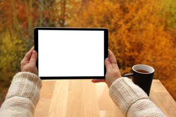 girl holds horizontally tablet PC with blank white screen, black mug with tea on the terrace over...