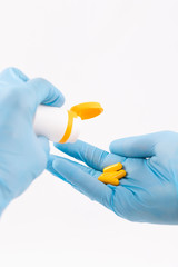 Doctor's hands, weared in blue gloves, holding bottle and yellow pills (closeup, vertical)