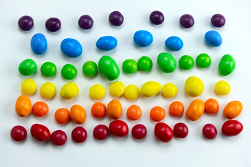 red, orange, yellow,green and blue candies rows on a white background top view flat lay, sweet rainbow