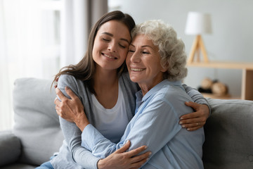 Affectionate young granddaughter and elderly grandma cuddling bonding at home