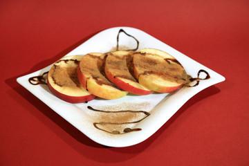 Plasterki jabłka z cynamonem i czekoladą na białym talerzu, dekoracja.