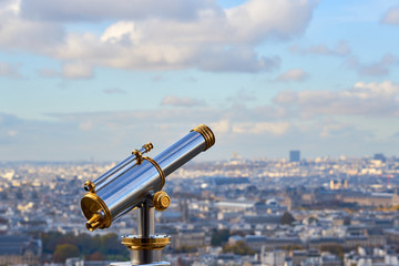 Telescope with blurred city of Paris, France on a background and blue sky with clouds. Copy space.