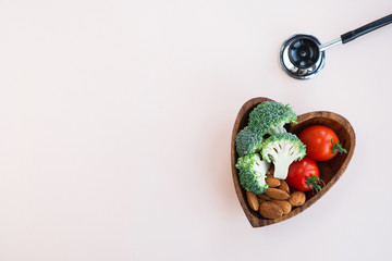Healthy food for heart on light background. Plate with vegetables, nuts and a medical stethoscope...