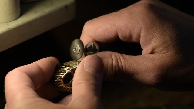 A jeweler is grinding a gold ring decorated with precious stones.