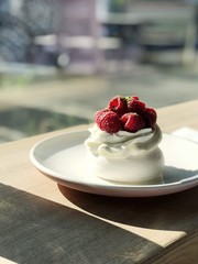 Merengue cake with a mascarpone and a raspberry lightened by bright sunlight