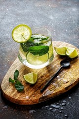 Water with a lime and a mint in the glass on the wooden cutting board