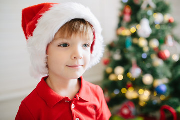 Portrait of a little cute boy with blue eyes in a Santa Claus hat in a decorated Christmas room...